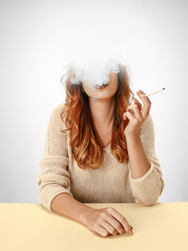 Tranquil woman sitting and smoking resting at the table. Cloud of smoke covering her face. Copy space