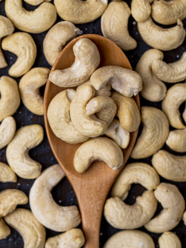 top view of a wooden spoon with salted roasted pistachios on black background